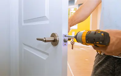Professional using power drill to install new door handle hardware on residential door